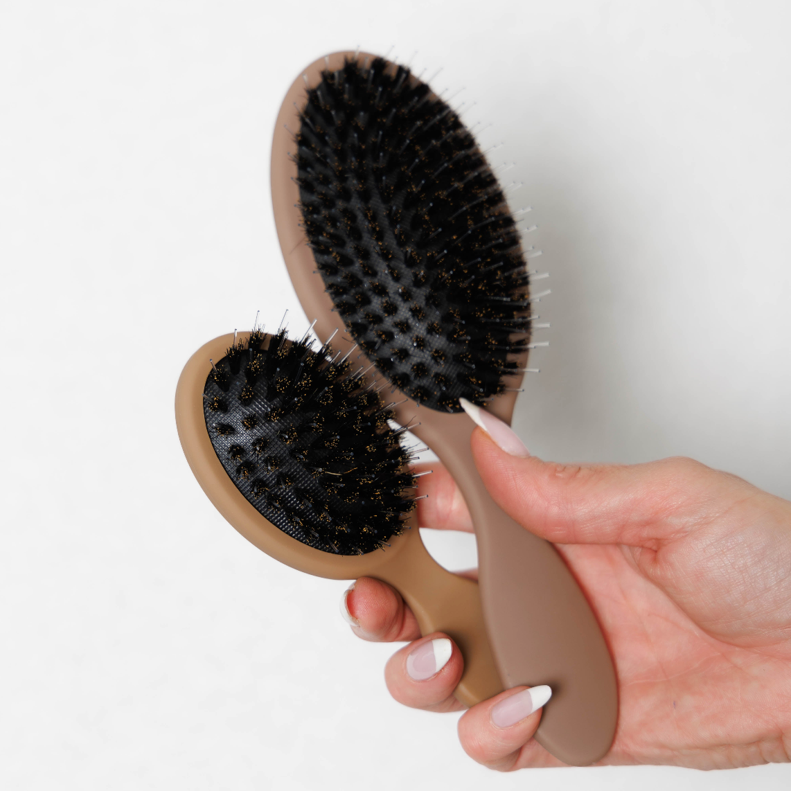 The Mane Baby Brush Duo held in hand, showing the bristle side of both the Original and Mini