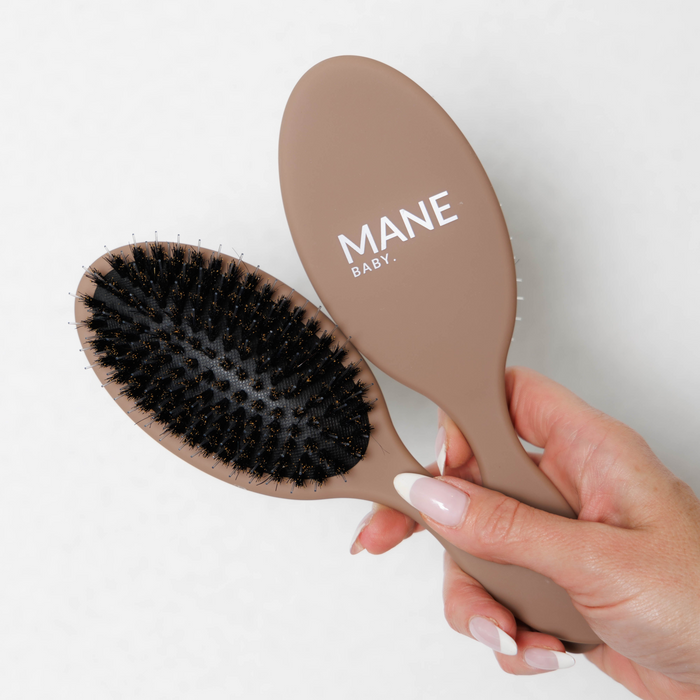 Mane Baby Original Boar Bristle Brush held in hand, showing both the branded back and the bristle side